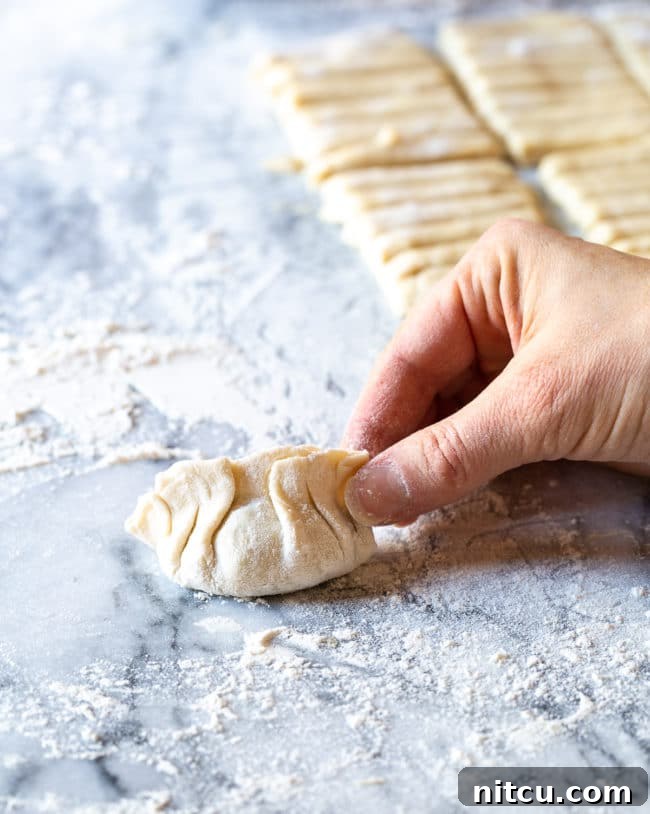 Hand pinching together dumpling with detailed folds. 