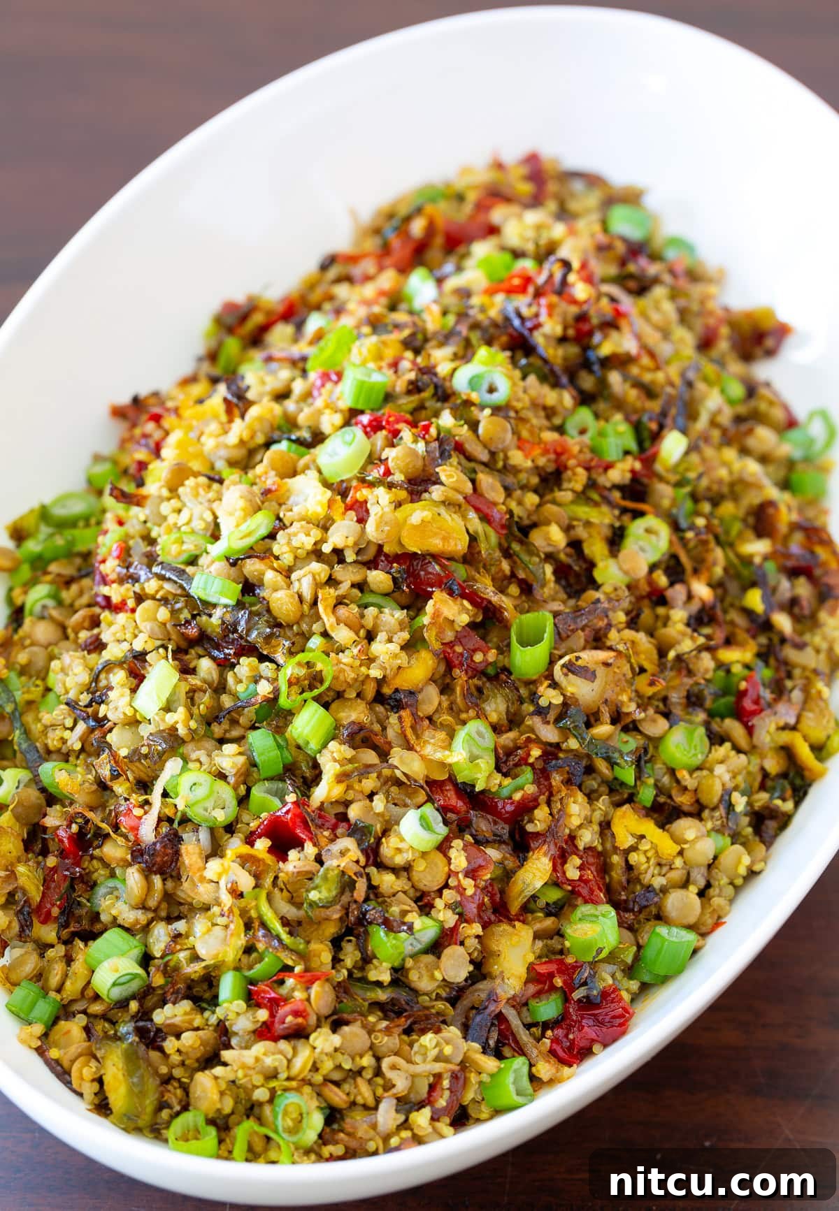 A vibrant quinoa lentil salad topped with roasted Brussels sprouts, shallots, and sweet red peppers, presented in a stylish bowl. Perfect for a healthy, filling meal.