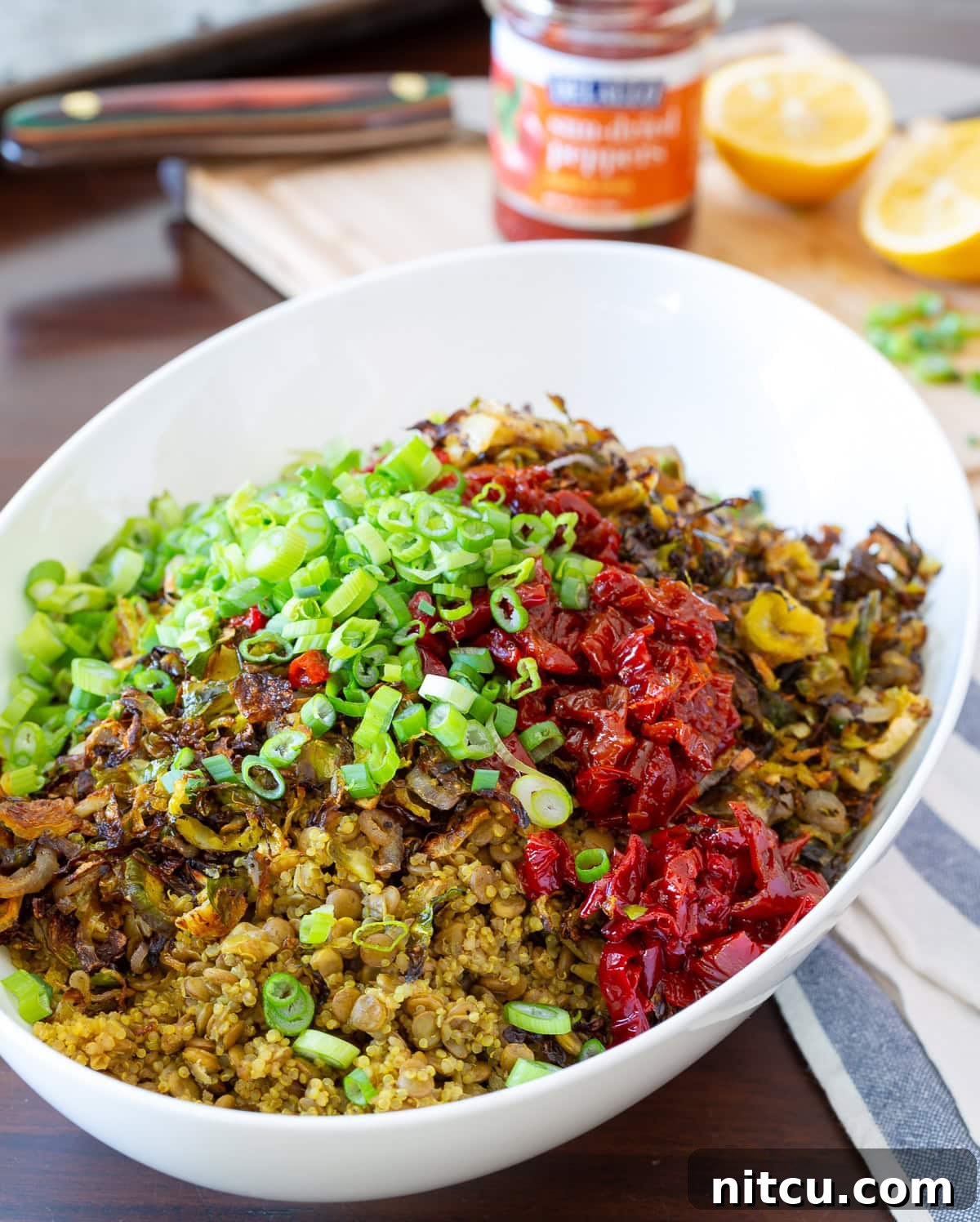 A stunning top-down view of the quinoa lentil salad in a white bowl, showcasing all the colorful ingredients: quinoa, lentils, roasted Brussels sprouts, red peppers, and scallions.