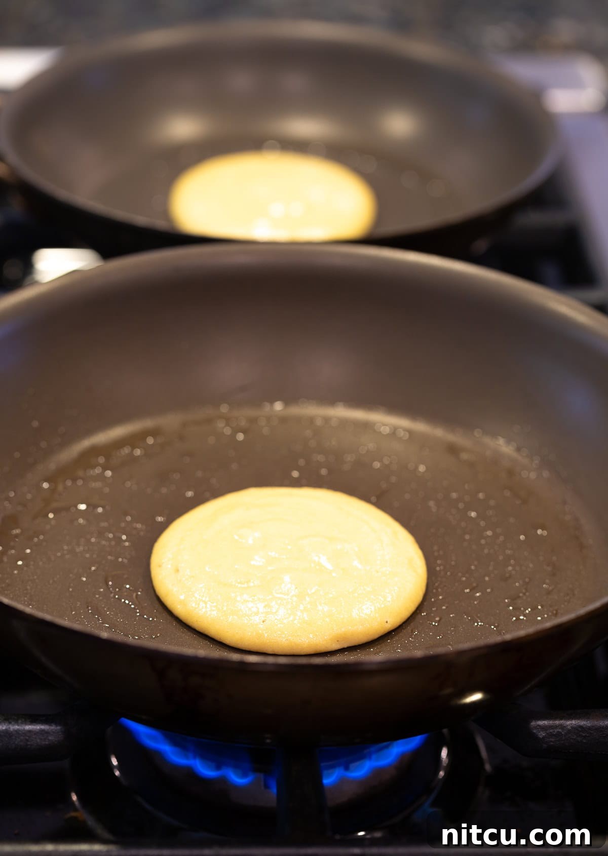 A golden-brown coconut flour pancake being cooked to perfection in a hot non-stick skillet on a stovetop, capturing the cooking process.