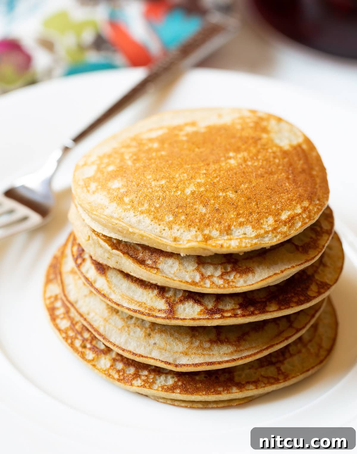 A stack of five golden-brown paleo pancakes on a white plate, subtly garnished, showcasing their inviting texture.