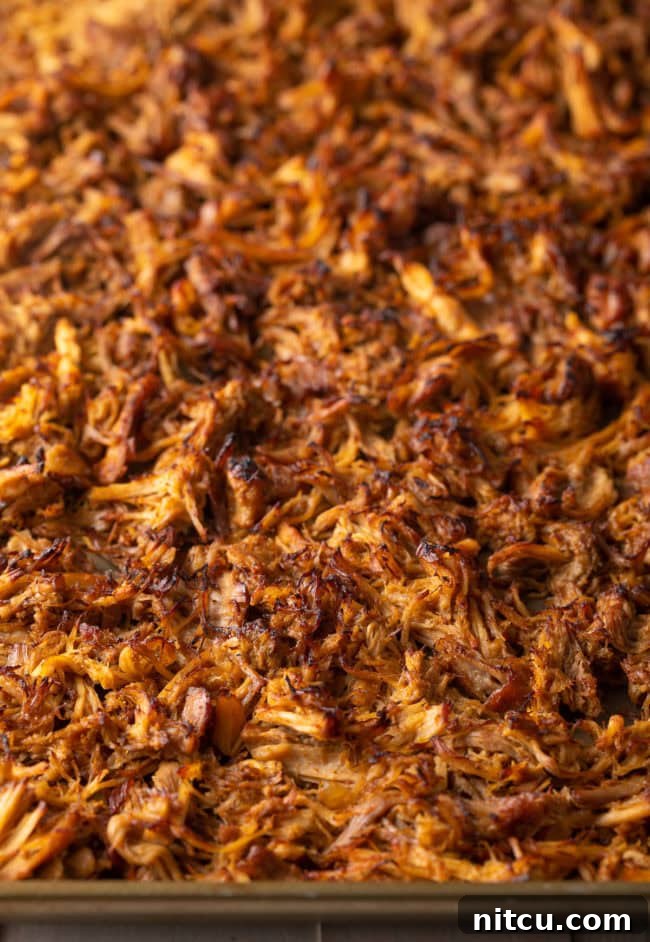 Broiled shredded carnitas on a baking sheet, displaying perfectly crispy and browned edges.