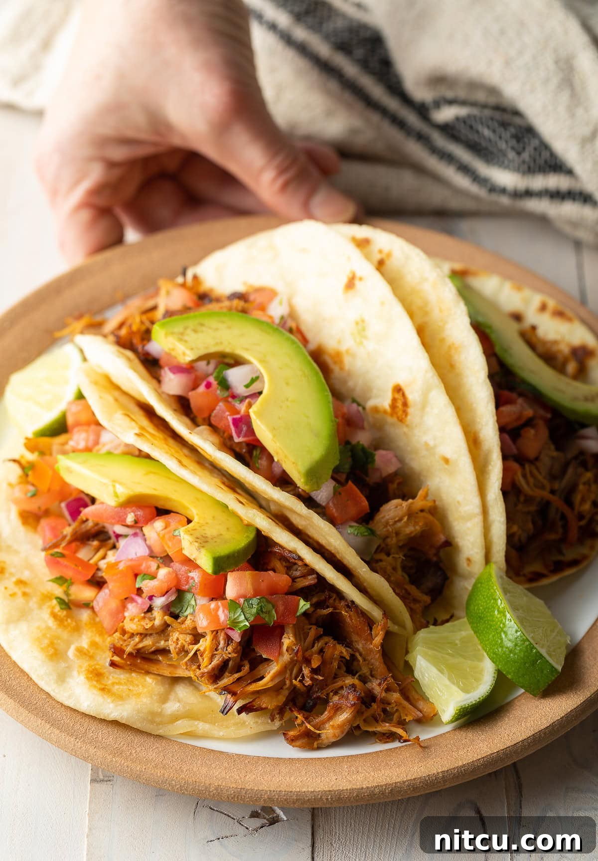 A hand reaching for a plate of mouthwatering carnitas tacos, highlighting the rich color and texture of the pork.