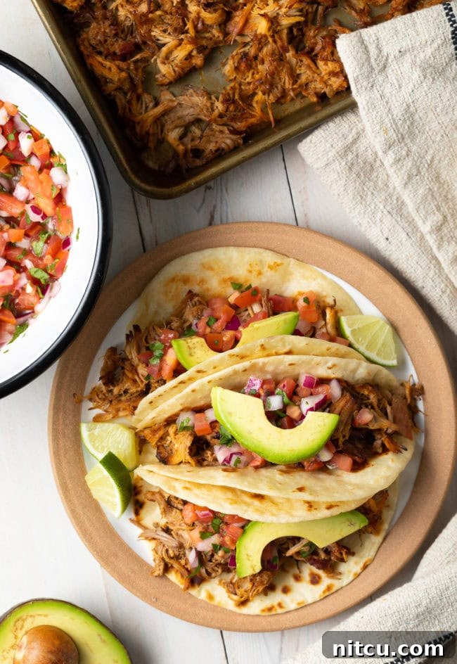 An overhead shot of plated slow cooker carnitas, garnished with fresh avocado slices and lime wedges, ready to be served.