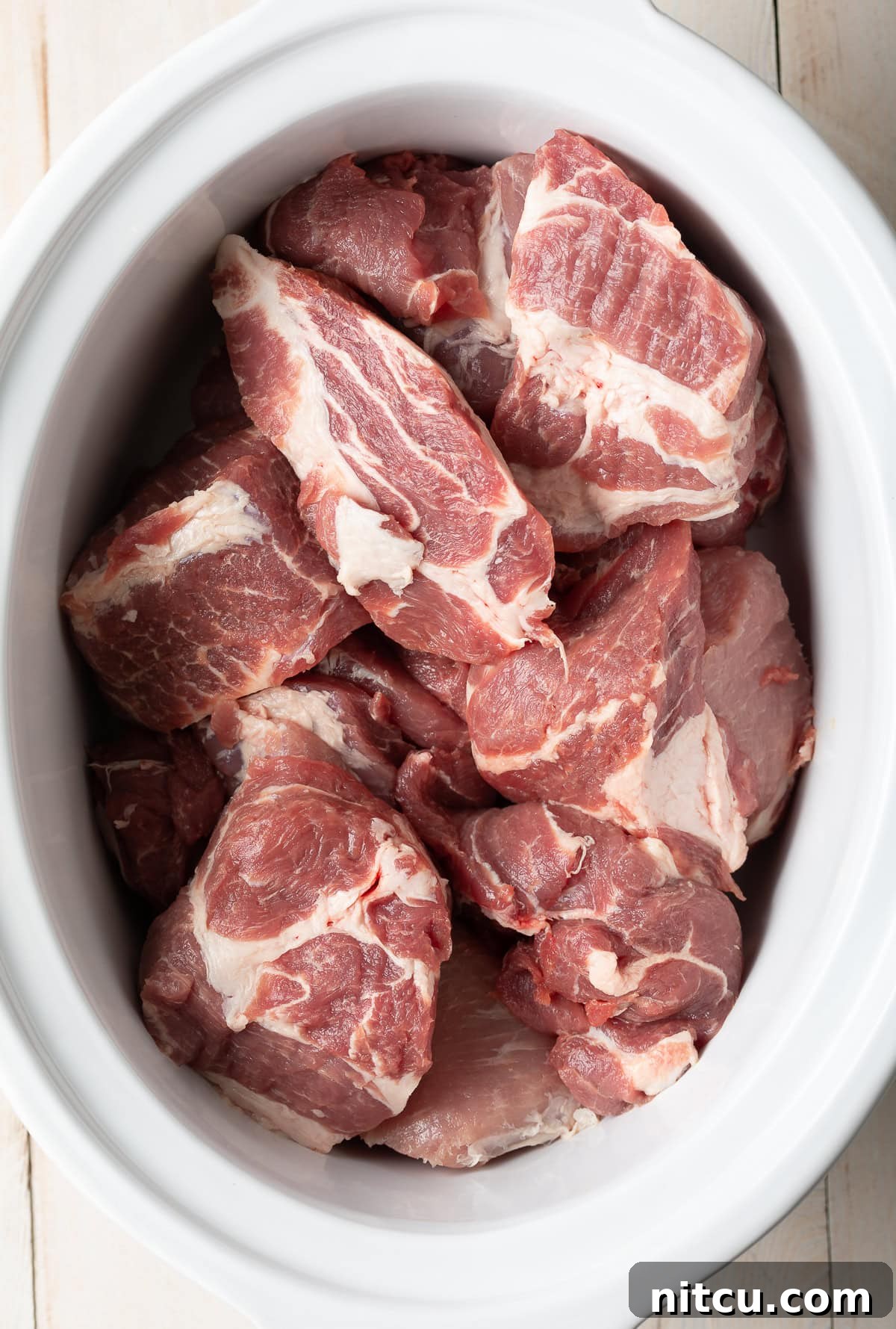 Large chunks of raw pork butt roast seasoned and ready for the slow cooker.