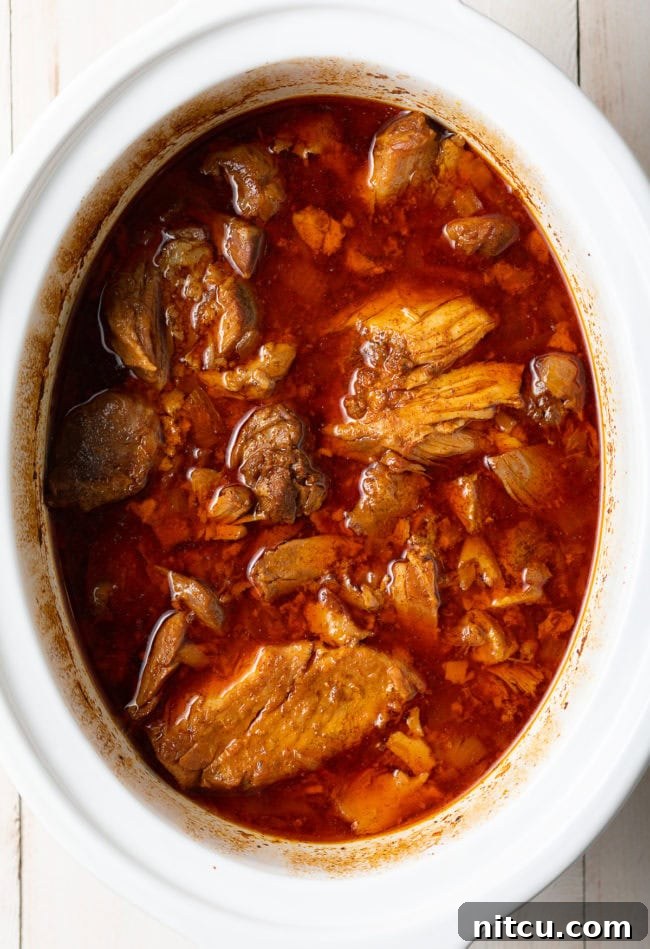 Pork carnitas after hours of slow cooking, appearing incredibly tender and juicy in the pot.