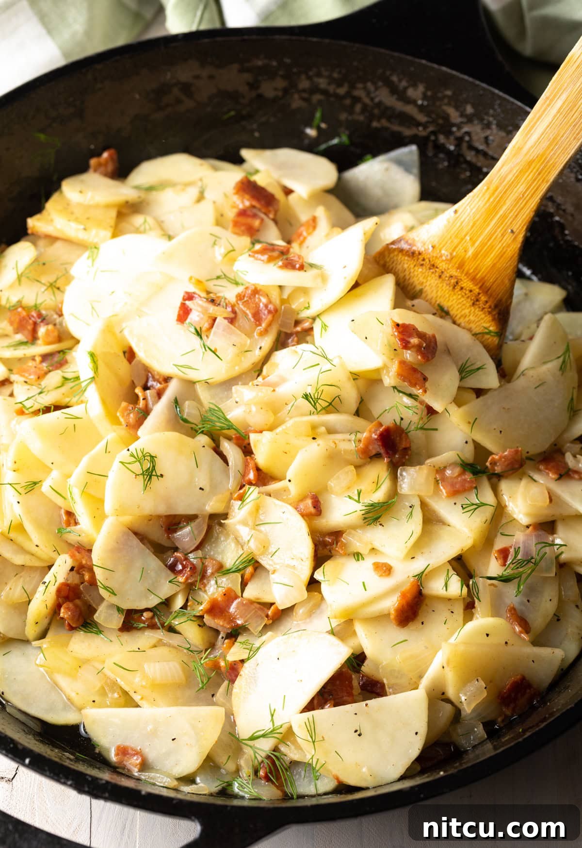 Potatoes, bacon, onions, and fresh dill gently cooking together in a large skillet, coated in savory bacon fat.