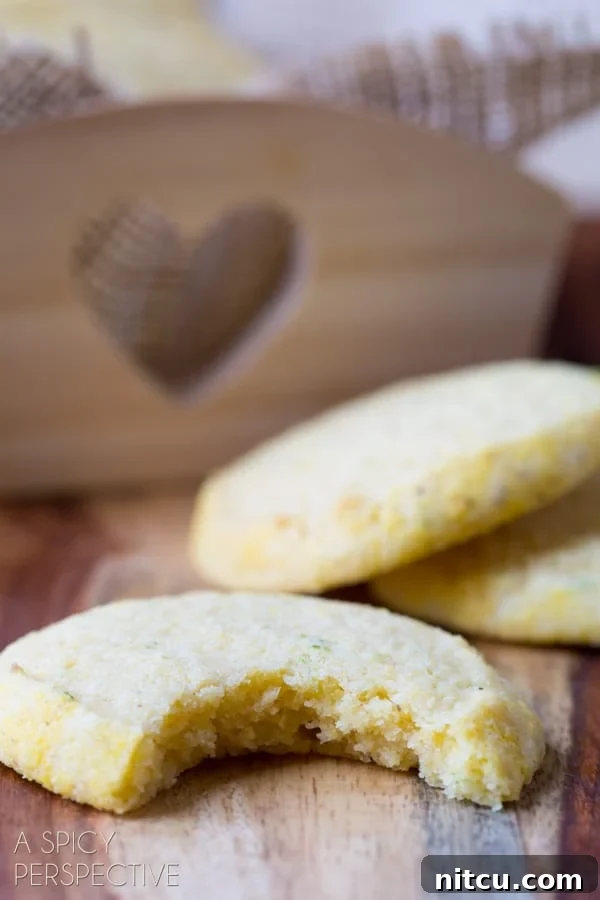 Closeup of a cornmeal cookie with a bite removed, revealing its tender interior and speckles of lime zest.