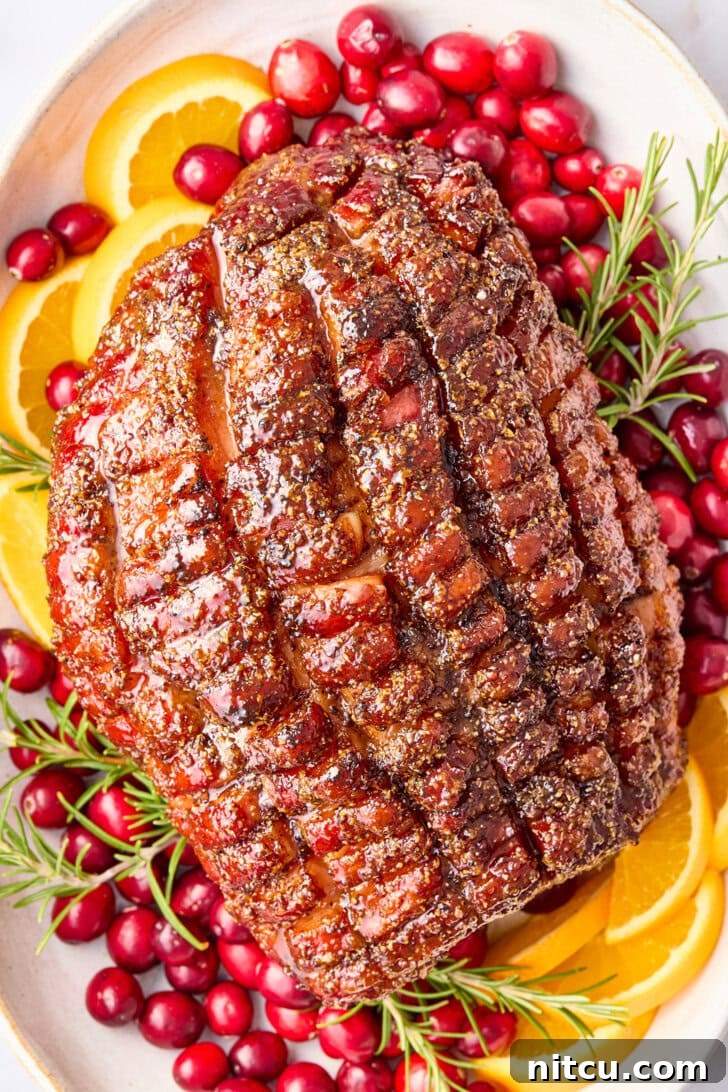 Overhead shot of perfectly baked brown sugar glazed ham on a festive serving platter, garnished with fresh cranberries, orange slices, and aromatic rosemary, ready to be carved for a holiday feast.
