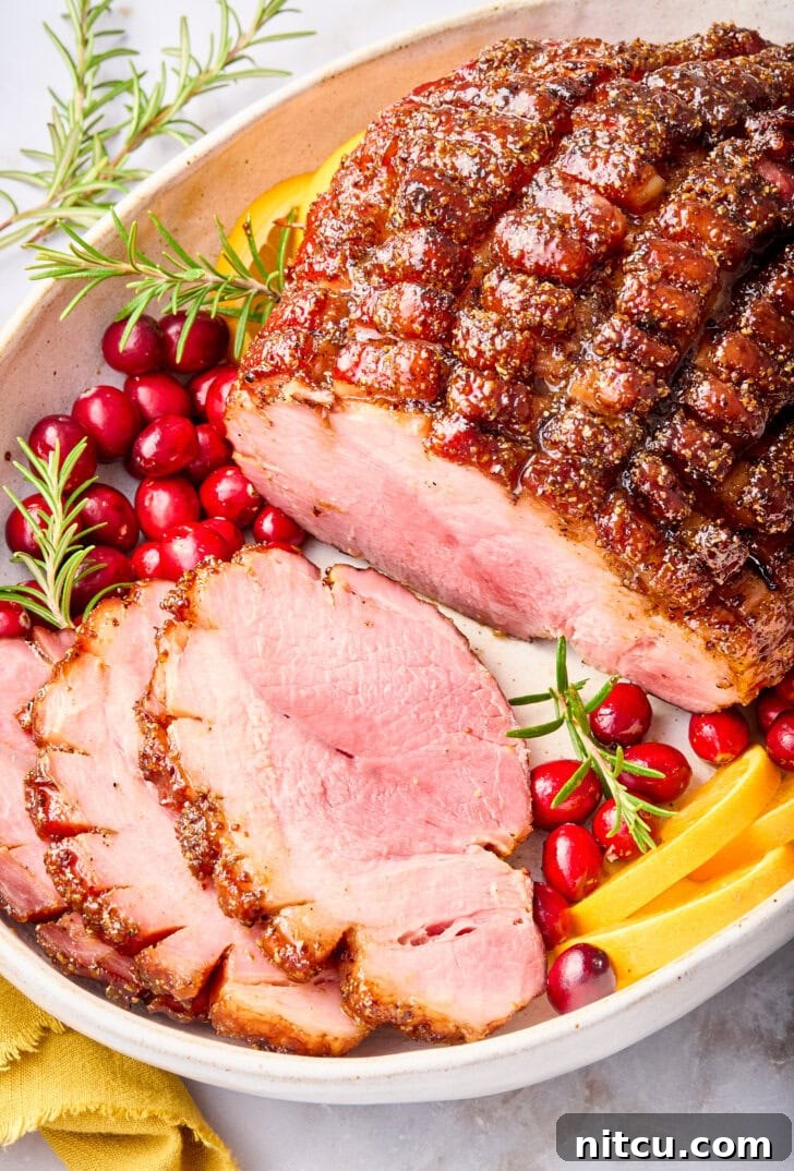 A large baked ham, beautifully glazed and partially sliced, presented on a serving platter, showing its juicy interior and caramelized crust.