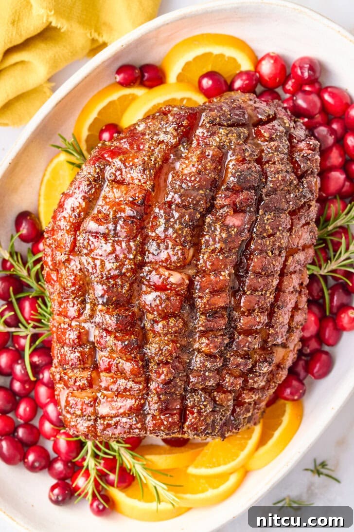 A fully baked Thanksgiving ham with brown sugar glaze, artfully arranged on a platter, adorned with fresh orange slices, vibrant cranberries, and aromatic herbs, creating a stunning visual display.