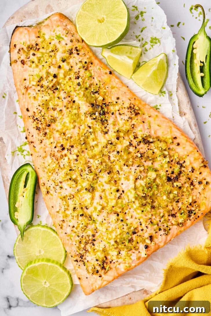 Overhead shot of perfectly oven baked salmon with fresh lime wedges and sliced jalapeño on top, ready to serve.