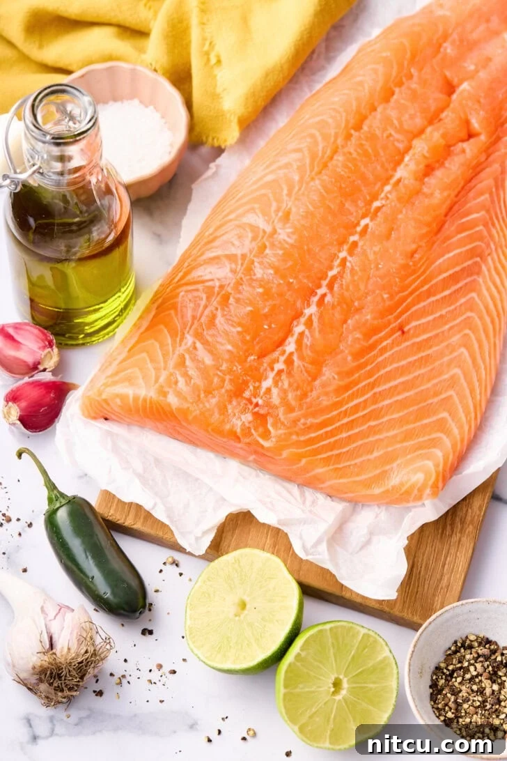 Key ingredients for oven baked salmon, including a salmon fillet, limes, garlic, and jalapeños, laid out on a baking tray.