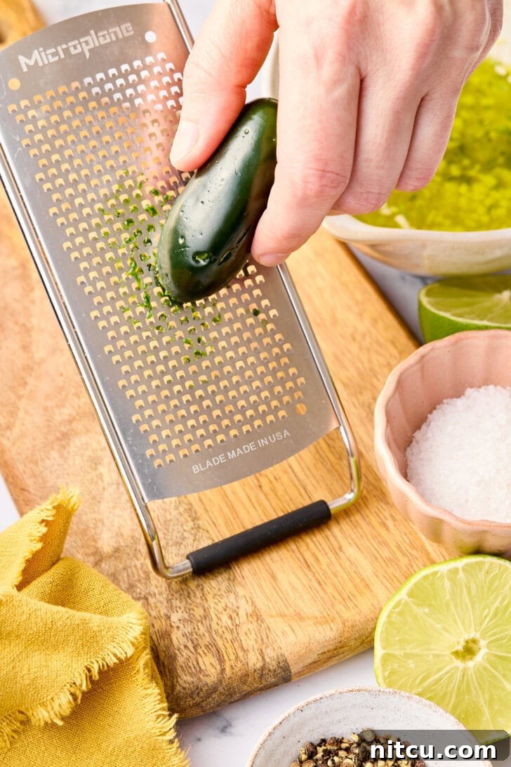 Grating fresh jalapeños directly into a bowl to create the flavorful marinade for the oven baked salmon recipe.