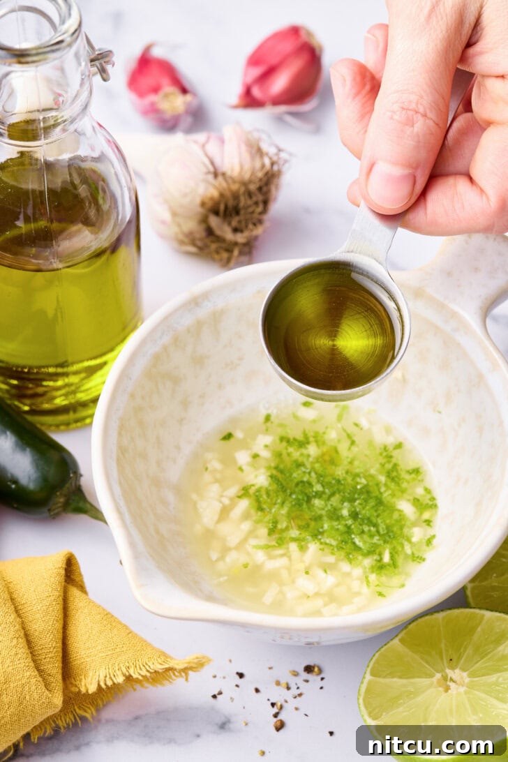 A small bowl showing olive oil being poured into a mixture of lime zest, garlic, and jalapeño, forming the marinade.
