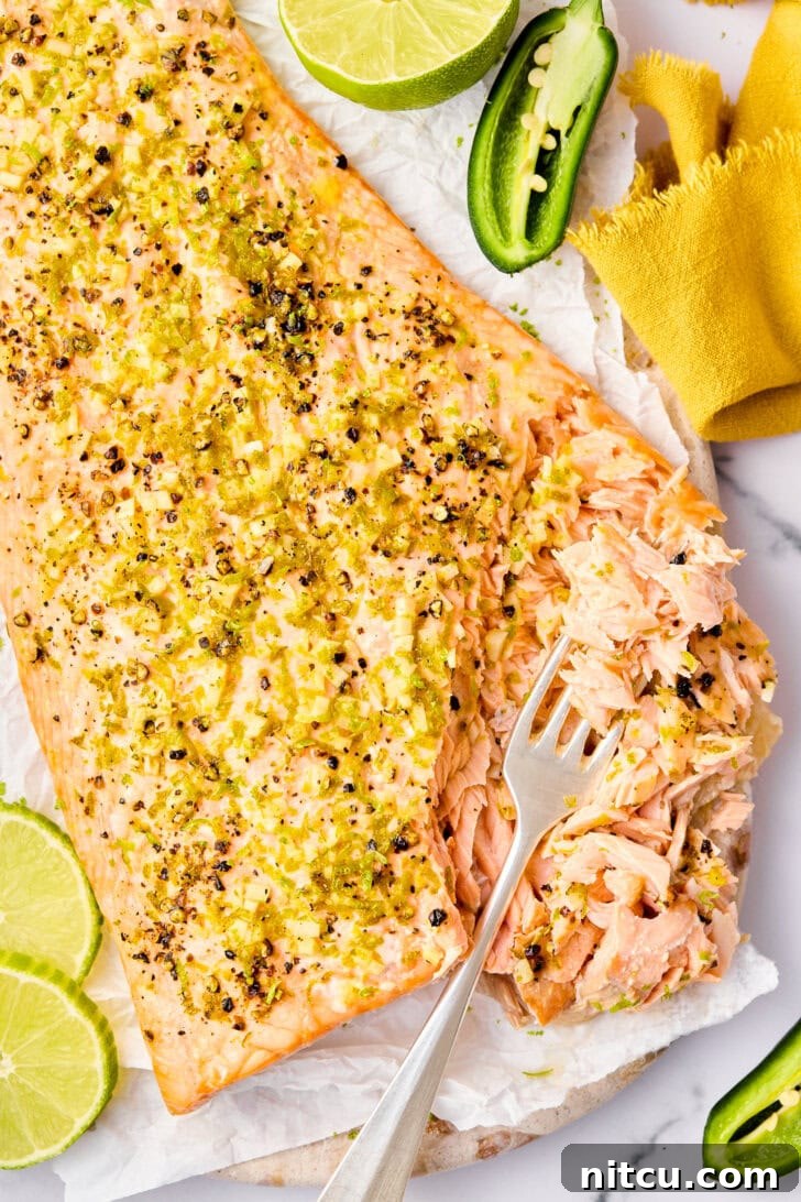 A close-up of oven-baked salmon, cut open with a fork to show its moist, flaky interior, garnished with spices.