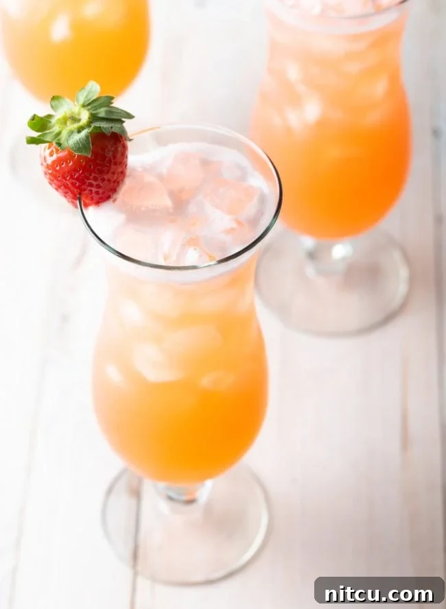 3 tall cocktail beverage glasses filled with strawberry pineapple agua fresca. Each class is garnished with a strawberry on the rim.