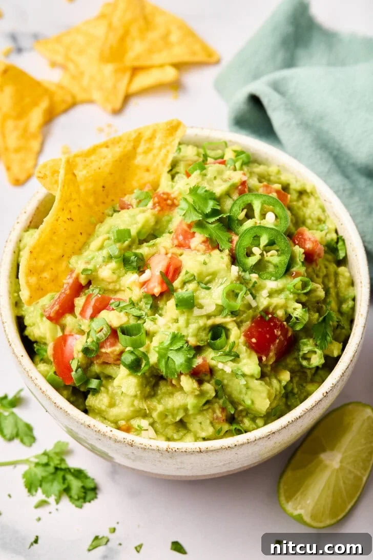 Freshly made guacamole topped with cilantro and diced tomatoes in a white bowl, surrounded by crispy tortilla chips.