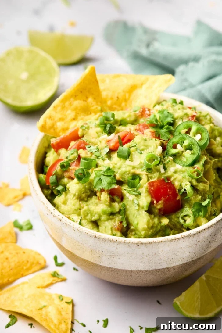 Crispy tortilla chips elegantly placed in a bowl of creamy guacamole, ready for dipping.