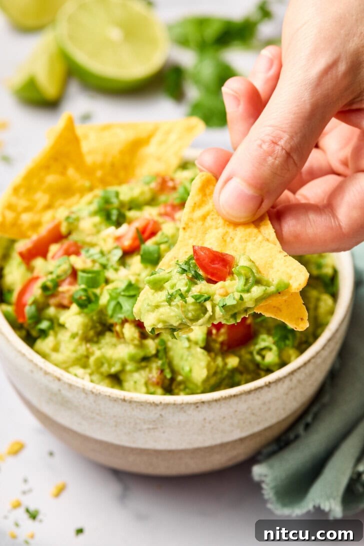 A hand scooping up a generous portion of creamy guacamole with a crispy tortilla chip.