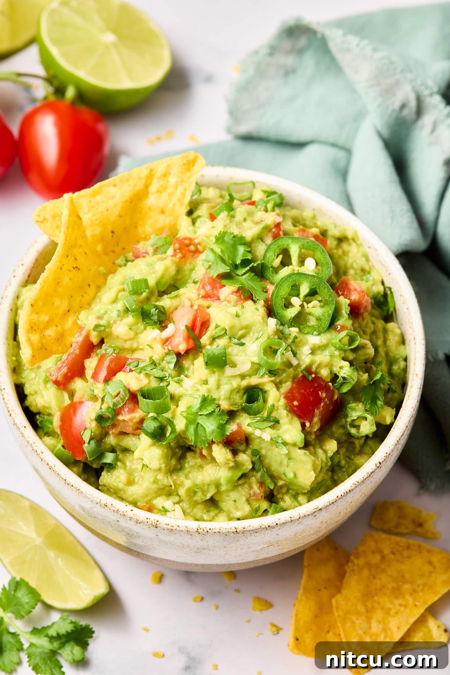 A bowl of guacamole garnished with a lime wedge, cilantro, and tomato, served with a side of tortilla chips.