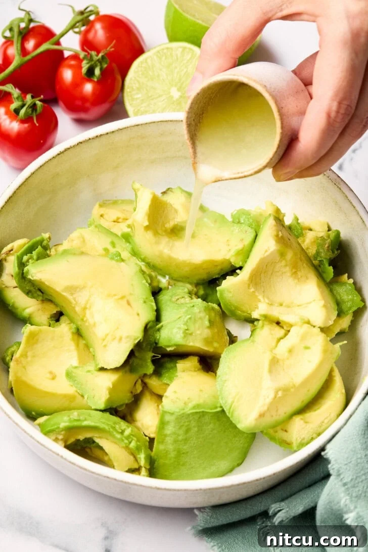 Chopped avocados in a bowl with a hand pouring fresh lime juice over them.