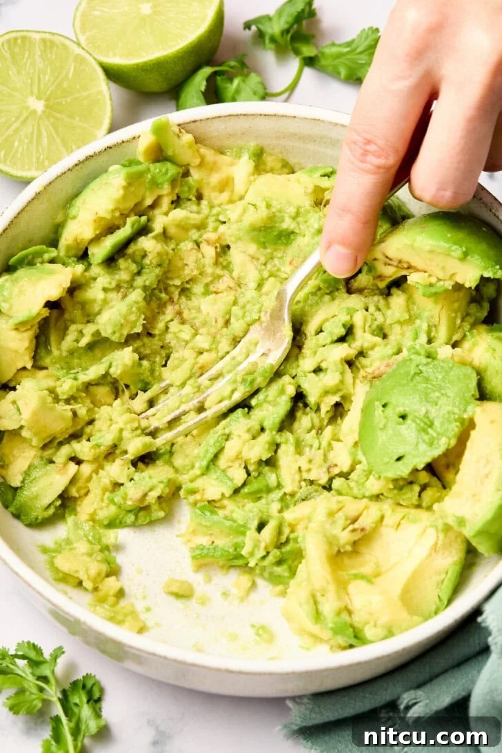 A fork mashing ripe avocado in a bowl to achieve the desired creamy consistency.