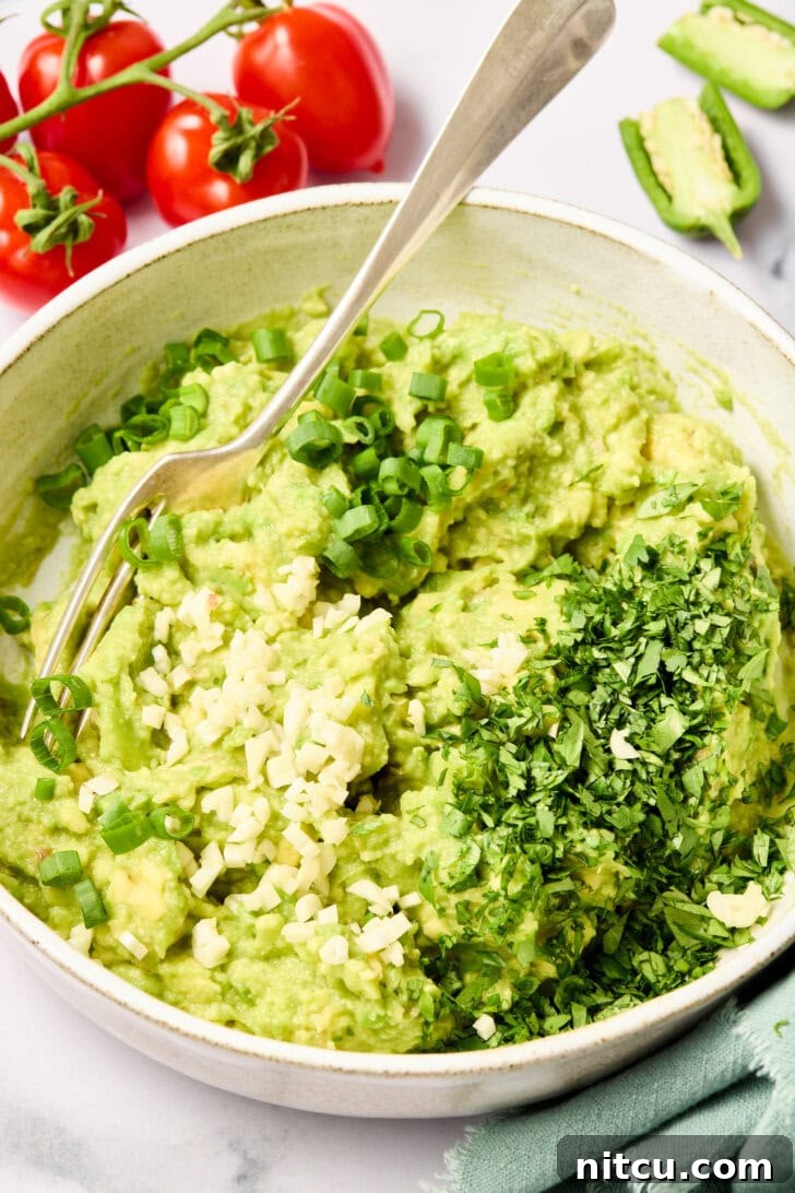 Fresh herbs and minced garlic being added to the smashed avocado mixture.