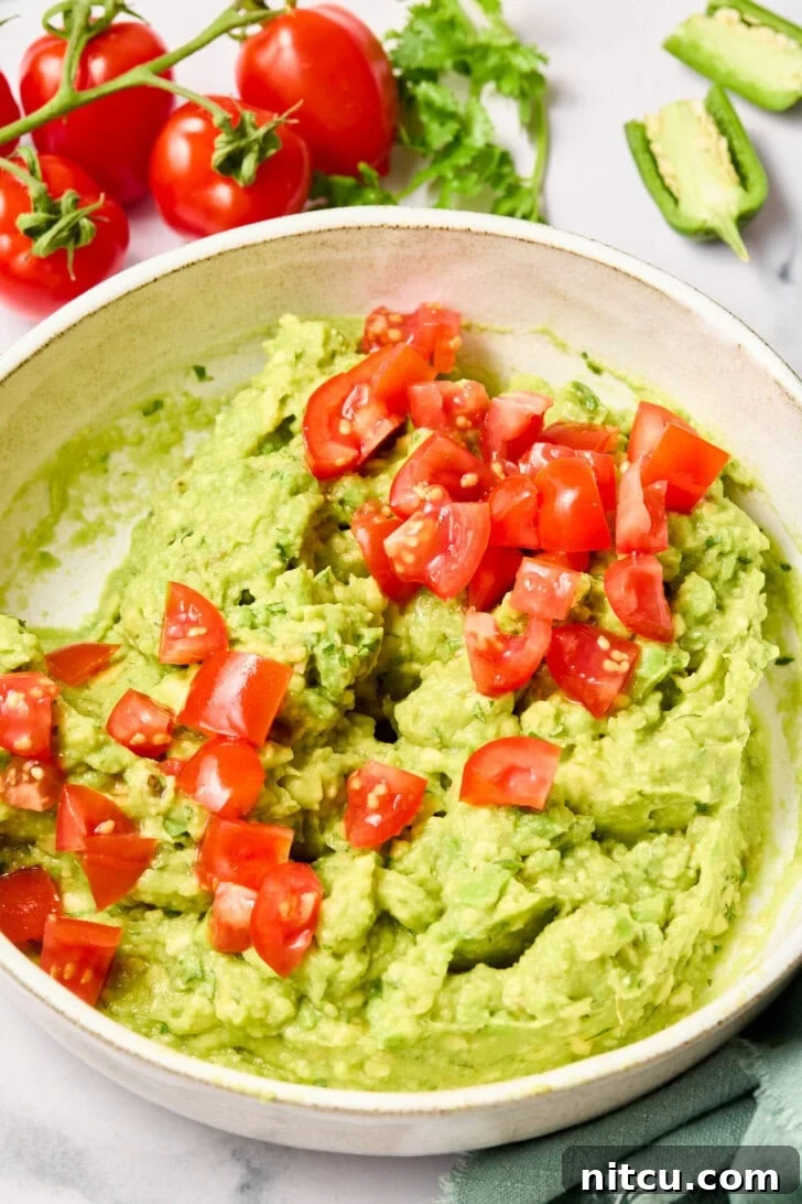 Diced tomatoes being gently mixed into the avocado mixture, adding color and texture.