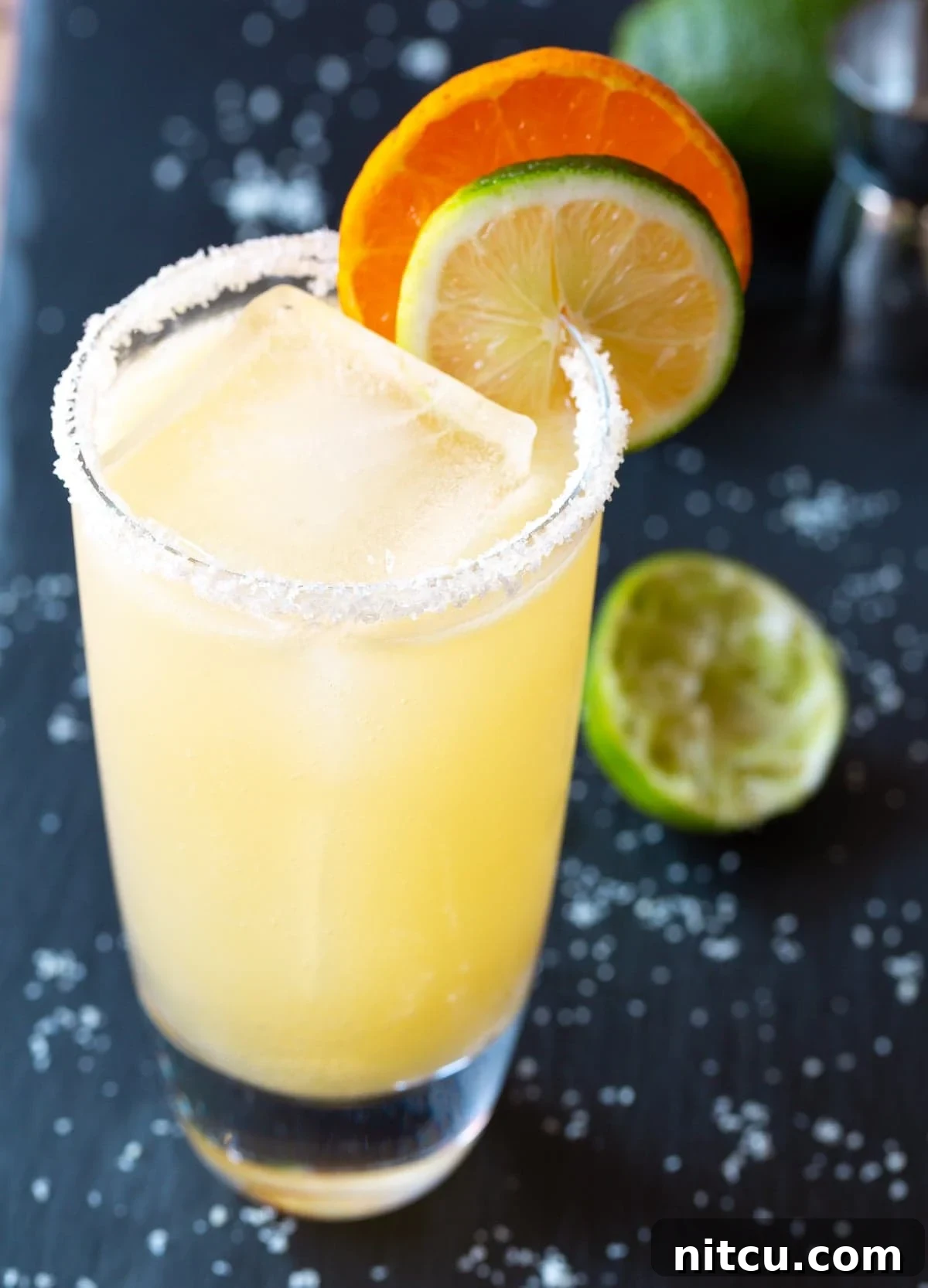 A vibrant margarita cocktail in a salt-rimmed glass, garnished with lime and orange slices, perfect for Cinco de Mayo celebrations.