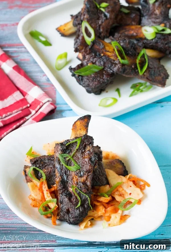 Asian beef ribs on a white plate with garnishes including kimchi and slivers of scallions. 