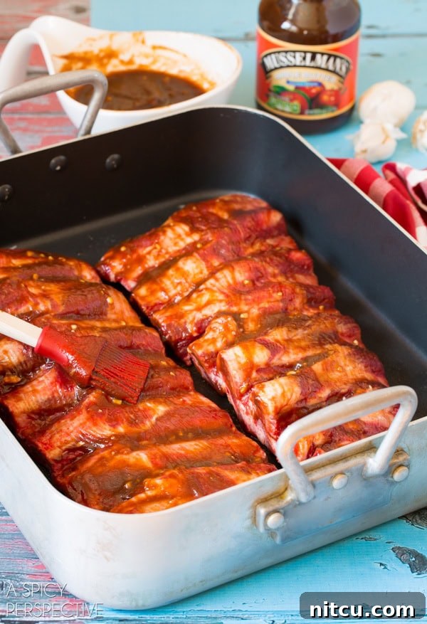 Beef ribs covered in cooking sauce sitting in baking pan with brush. 