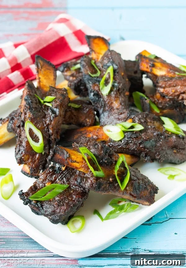 Closeup of cooked Asian beef ribs on white serving plate topped with slivers of fresh scallions. 