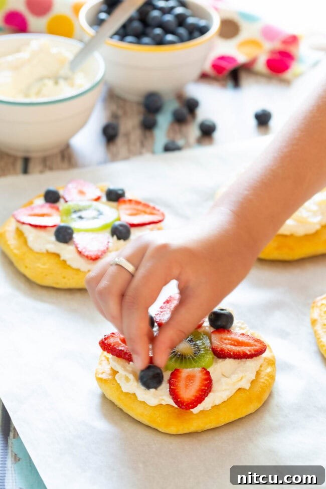 Easy Fruit Pizza for Breakfast being assembled, with fresh fruit being added to the cream cheese topping.