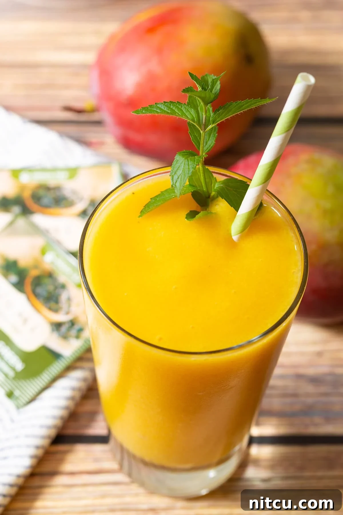 A vibrant mango green tea smoothie in a glass, garnished with fresh mint and a stylish straw. The texture is creamy and inviting, promising a refreshing and healthy start to the day.