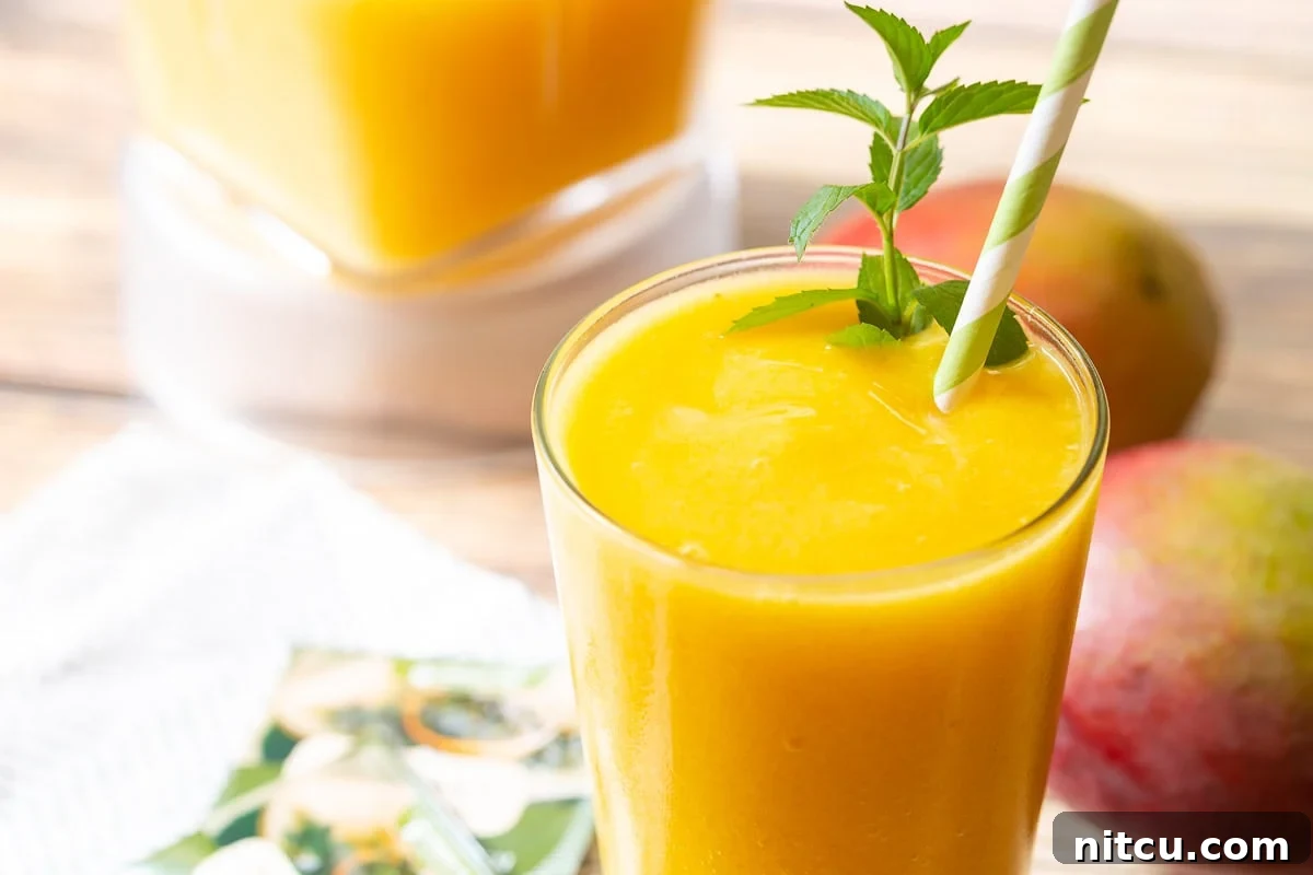 A beautifully presented Mango Green Tea Smoothie in a clear glass, garnished with fresh mint and a striped straw, invitingly ready to be enjoyed.