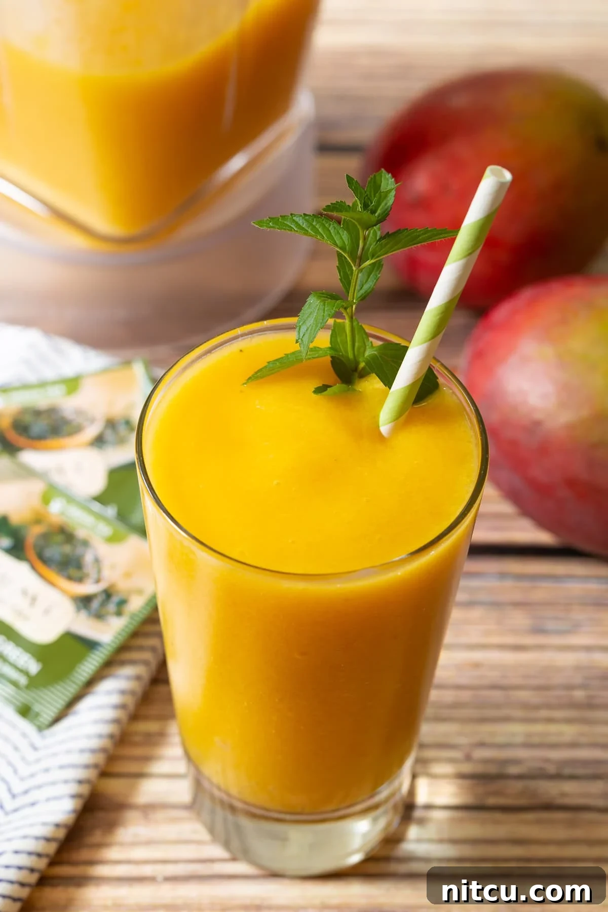 Close-up view of a full glass of Mango Green Tea Smoothie, garnished with mint and a green and white straw, showcasing its vibrant color and smooth texture.