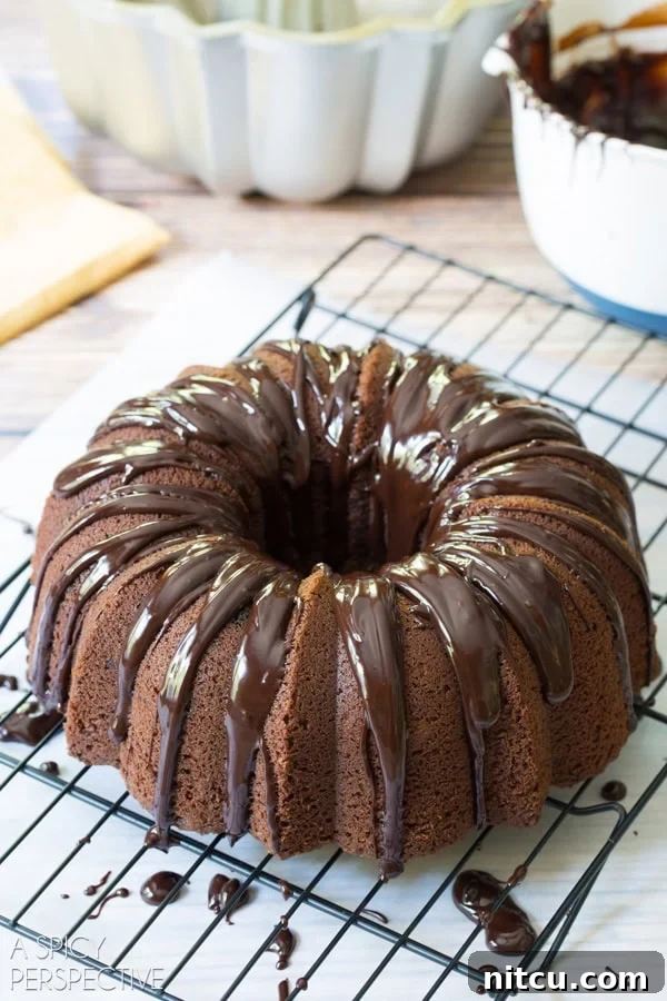 A Baileys Irish Cream Bundt Cake artfully drizzled with glossy chocolate ganache and golden caramel, cooling on a rack.
