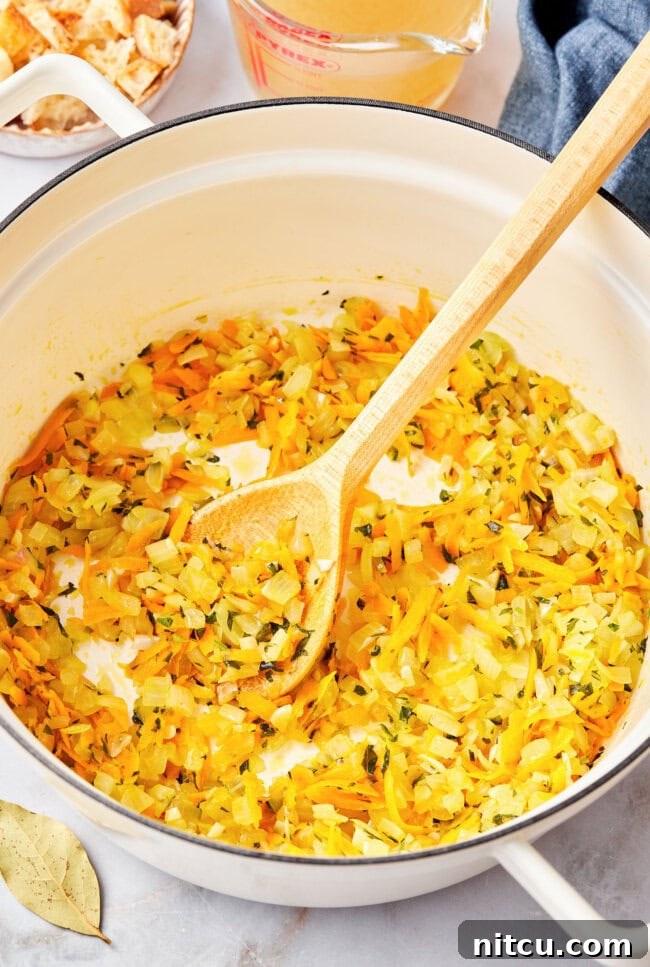 Chopped onions, garlic, and carrots sautéing in olive oil in a large saucepot.