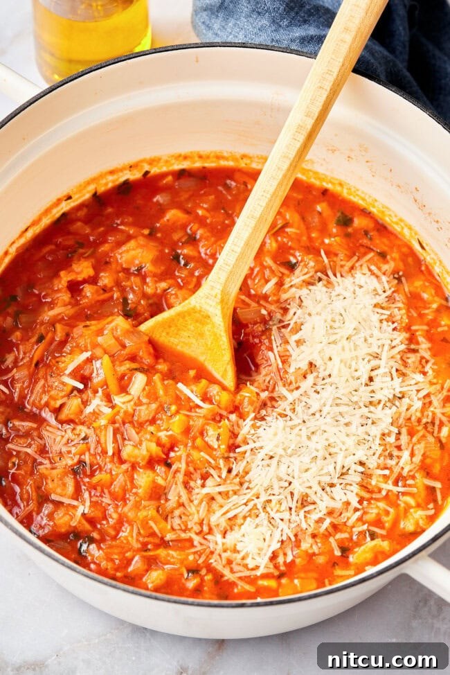 A pot of Pappa al Pomodoro simmering, with Parmesan cheese being added and stirred in.
