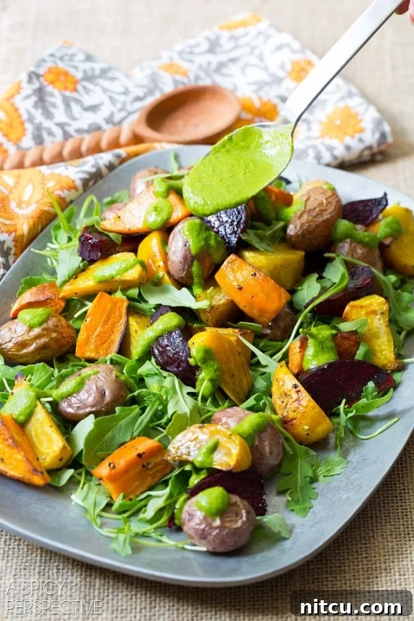 A hand drizzling homemade cilantro dressing over the roasted root salad on a serving platter.