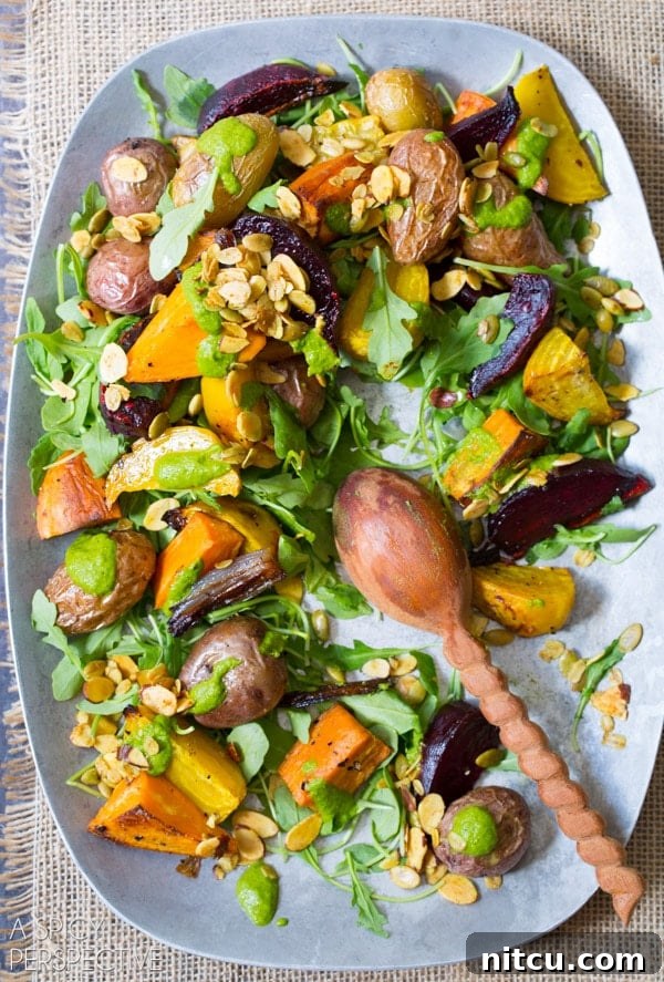 A top down view of roasted vegetable salad on a serving platter. A wooden spoon is resting on the platter where a few servings of the salad are missing.