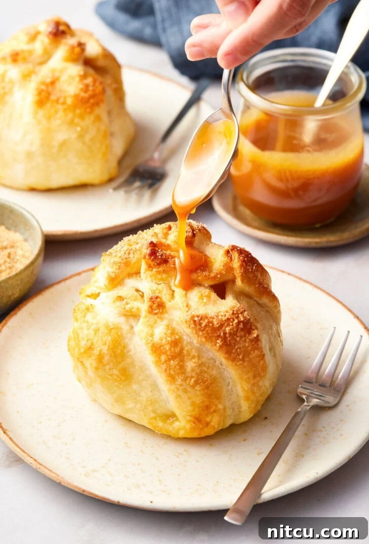 Finished mini apple pie bomb on a plate with caramel being drizzled on top with a spoon.