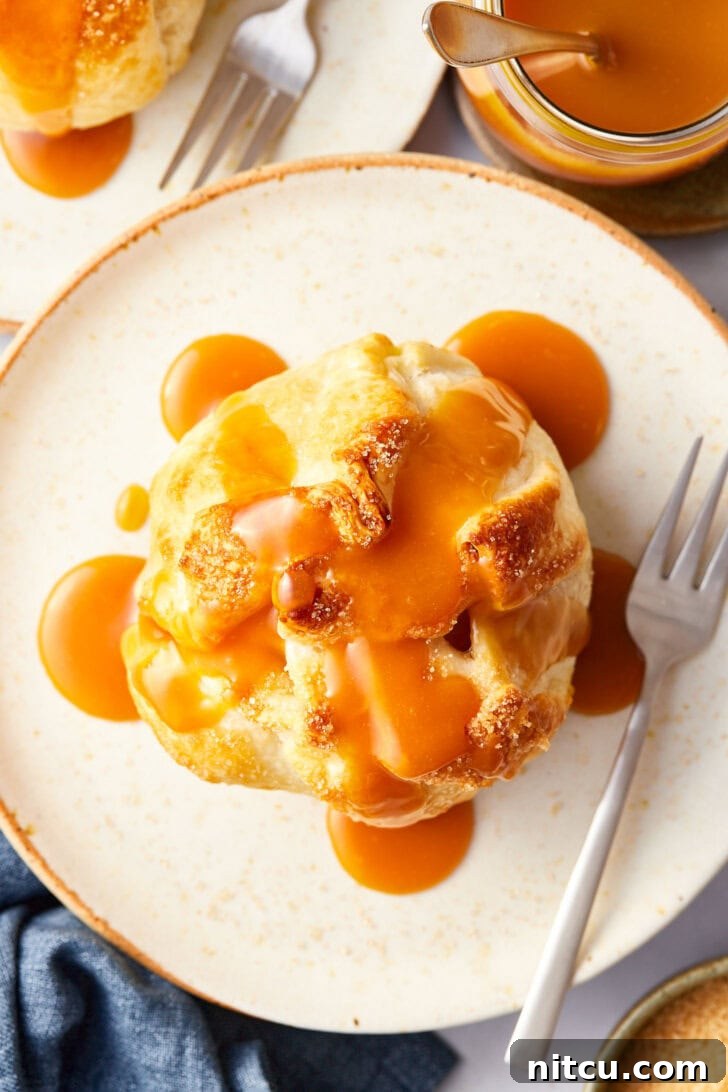 Baked apple wrapped in puff pastry on a plate with caramel drizzled on top. 