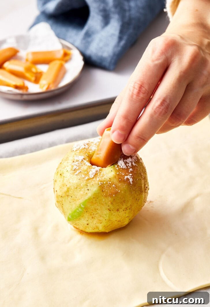 Peeled apple being stuffed with caramel candy for apple pie bombs.