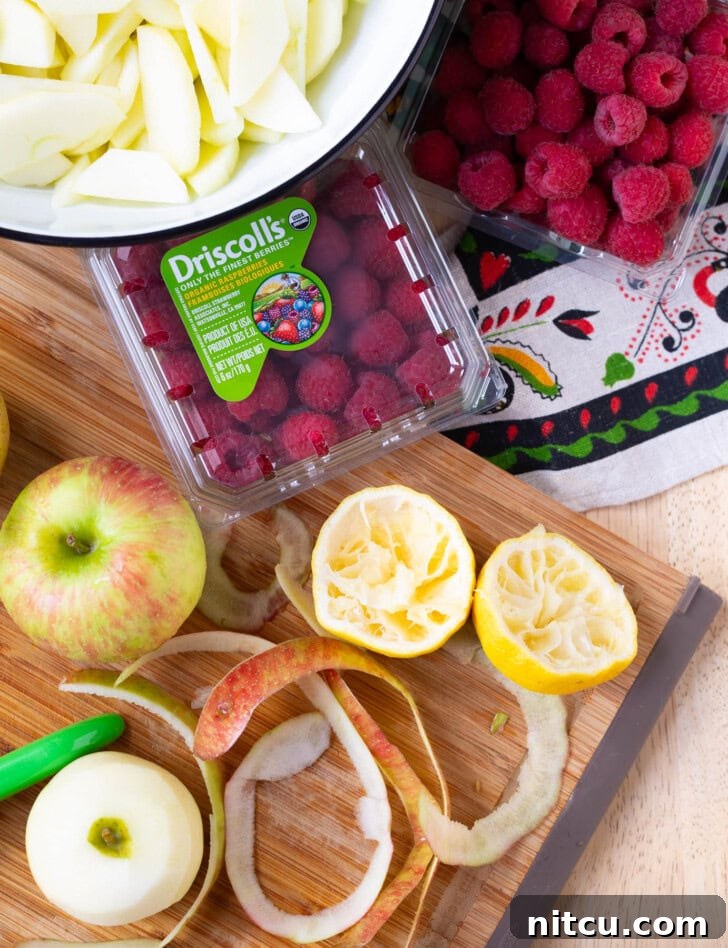 Overhead shot of fresh ingredients laid out for making apple pie, including apples, raspberries, and spices.