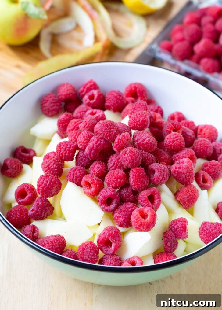 Bowl filled with sliced apples and fresh raspberries, tossed together for the pie filling.