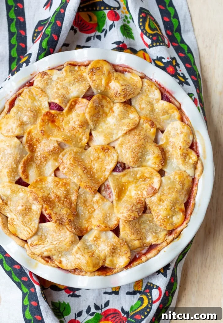 A whole Raspberry Apple Pie, perfectly baked with a golden crust and intricate top design, ready to be served.