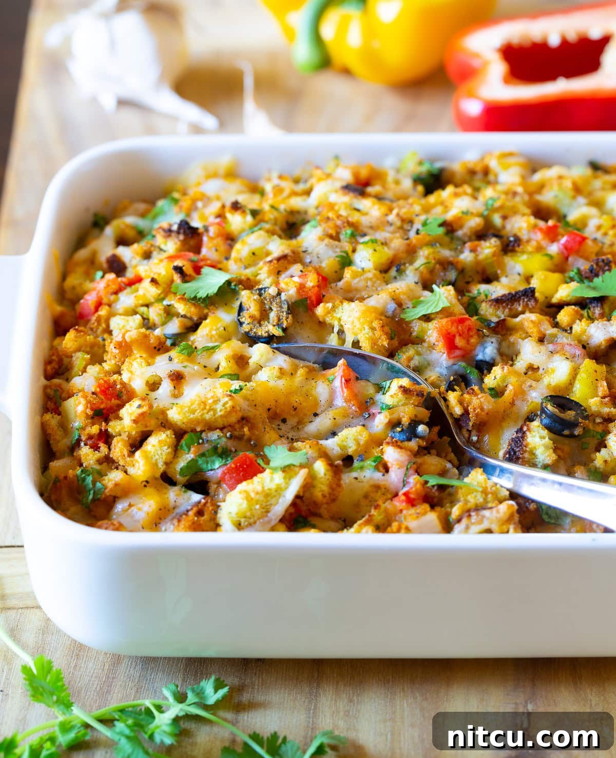 Cornbread Stuffing Recipe - Mexican Thanksgiving version with vibrant chiles and melted cheese in a baking dish, served with a spoon