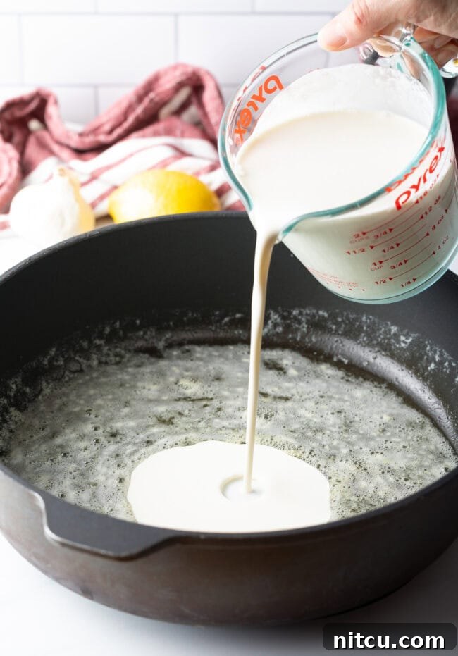 Heavy cream gently simmering in a pan, forming the base for Alfredo sauce